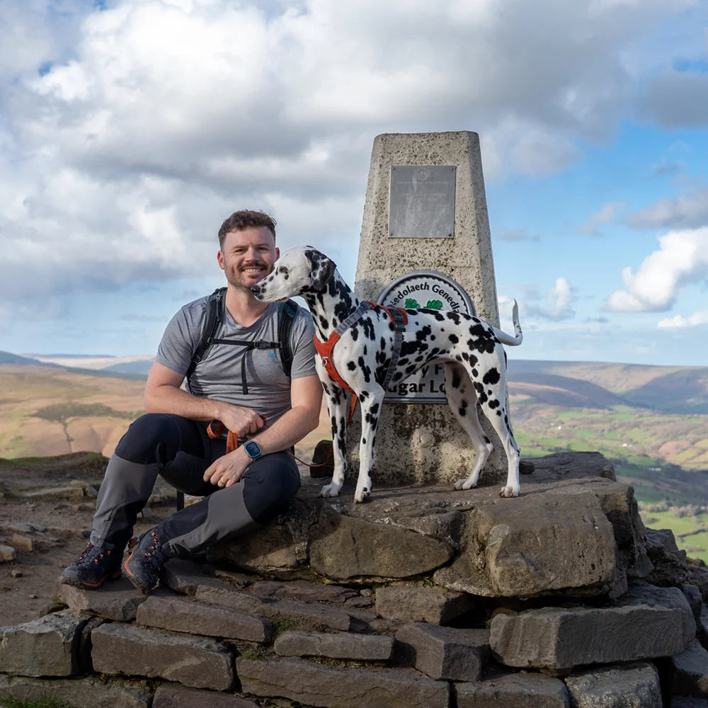Man with a Dalmatian dog at a stone monument with a scenic background
